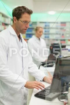 Pharmacist Using Computer At Counter