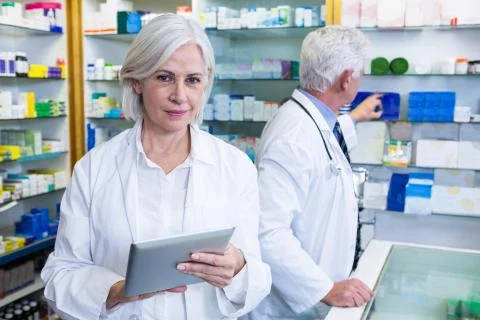 Pharmacist using digital tablet and co-worker checking medicines Fotos de archivo