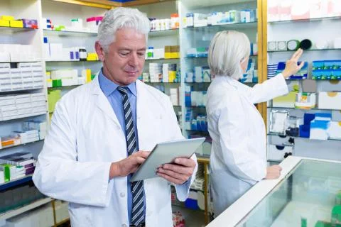 Pharmacist using digital tablet and co-worker checking medicines Stock Photos