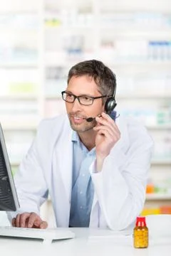 Pharmacist wearing headset while using computer at counter Stock Photos