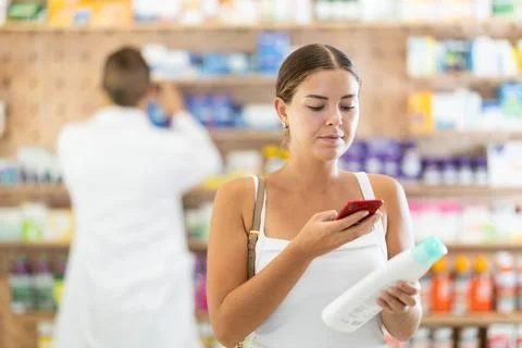In pharmacy girl customer scans code on shampoo label, photographs packaging. Stock Photos