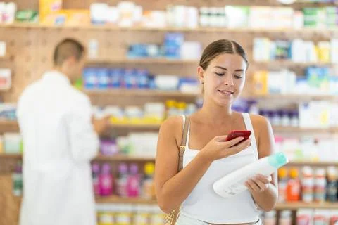 In pharmacy girl customer scans code on shampoo label, photographs packaging. Stock-Fotos