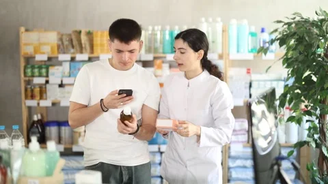 In pharmacy, guy scans barcode on antitussive syrup. Girl pharmacist offer help Stock Footage 318432648