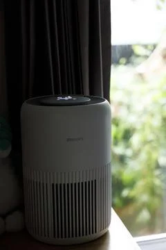 Philips air purifier placed on windowsill with black curtains beside it Stock Photos