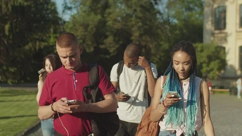 Phone addicted diverse students walking on campus Stock Footage 109158179
