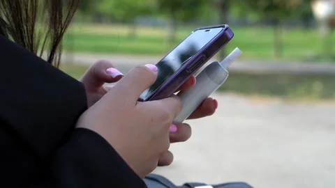 A phone and an electronic cigarette in the hands of a young woman. Stock Footage 288712469