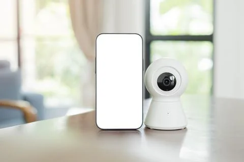 A phone with blank screen setting next to a small surveillance camera on th.. Фото