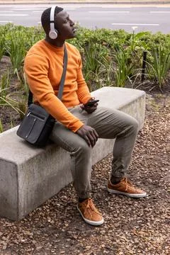 Phone buzzing, man sitting on bench, wearing headset, holding phone, tilting Stock Photos