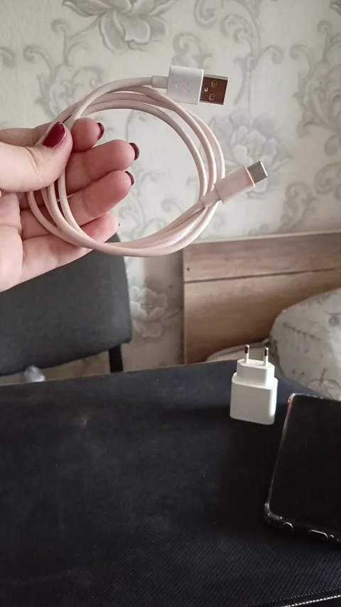 A phone cable in a womans hand, a charging unit and a phone on the table. Phone Stock Footage 319980606