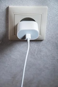 Phone charger in an electrical socket on the wall, close-up, vertical photo Stock Photos