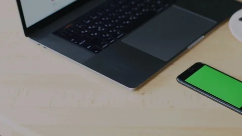 Phone with chromakey lying on table behind laptop and cup of coffee Stock Footage 113864555
