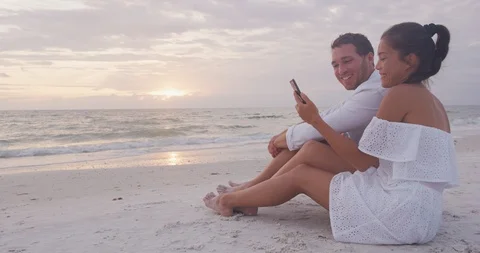 Phone - couple using smartphone app having fun laughing on romantic beach Stock Footage 103549819