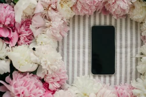 Phone with empty screen and peonies frame flat lay on rustic table cloth. Spa Stock Photos