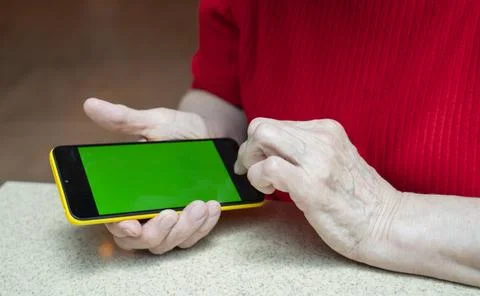 Phone with a green screen in the arm of an elderly woman of retirement age. Stock Photos