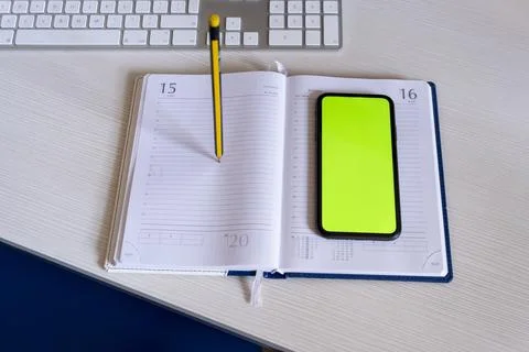 Phone with a green screen is on the notebook, and a computer keyboard Stock Photos