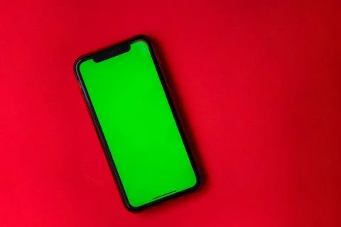 A phone with a green screen is on a red background. Stock Photos