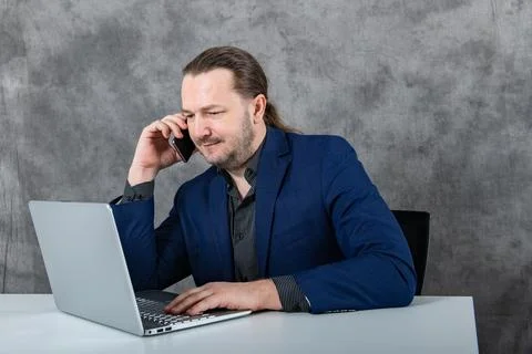 On the phone, a man in a jacket talks and works at a laptop Stock Photos