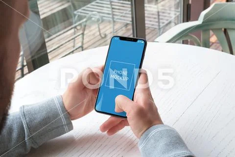 Phone mockup in man hands. White wooden coffee shop desk in background PSD-Vorlage