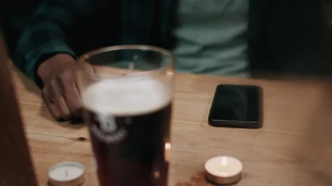 Phone notification on the table behind blurred beer glass inside a pub Stock Footage 132016194