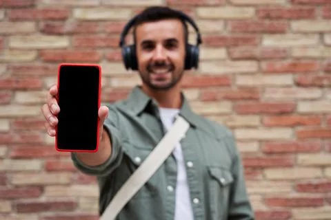 Phone screen for copy space held by a blurry cheerful man next to a brick wall. Stock Photos