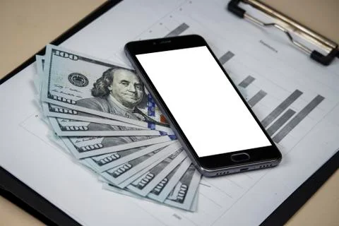The phone with a white screen is on dollars with sheets with charts. Template Stock Photos