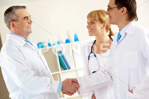 Photo of aged physician and young clinician looking at each other while handshak Stock Photos