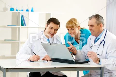Photo of aged physician pointing at laptop display with two colleagues near by l Stock Photos