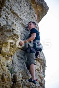 Photo of athlete man in helmet clambering over rock against background of green Stock Photos