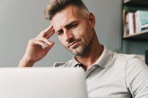 Photo of brooding adult man using laptop while working in apartment Stock Photos