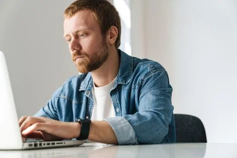 Photo of brooding handsome man working on laptop while sitting at table Stock Photos
