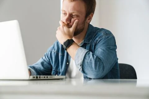 Photo of brooding handsome man working on laptop while sitting at table Stock Photos