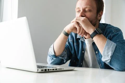 Photo of brooding handsome man working on laptop while sitting at table Stock Photos