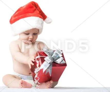 Photo of curious and surprised baby in santa cap looking at giftbox in his hands Stock Photos