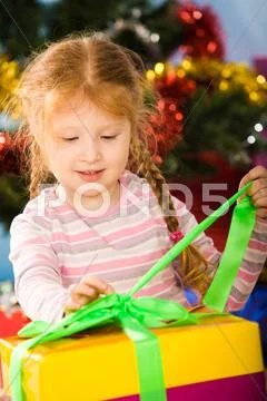 Photo of curious girl undoing green ribbon on giftbox to find her present Stock Photos
