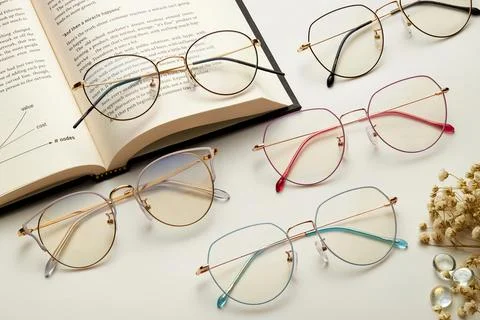 Photo of eyeglasses of different frames with an open book and a plant on white Stock Photos