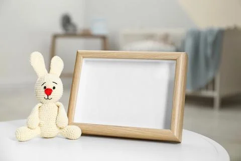 Photo frame and toy bunny on table in baby room interior. Space for text Stock Photos