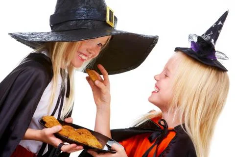 Photo of girl in halloween costume with tray of bisquits offering one to her twi Stock Photos