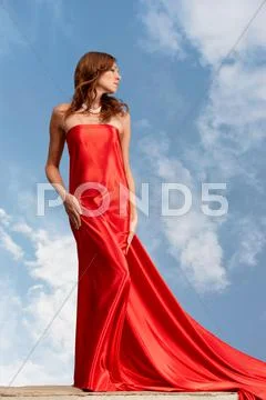 Photo of graceful female folded in bright red silk shawl with cloudy sky at back Stock Photos