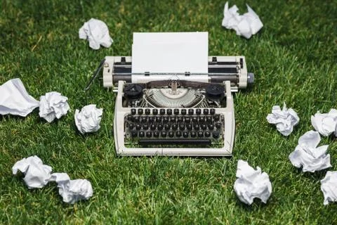 Photo of old typewriter on a green grass with a sheet of paper. Stock Photos