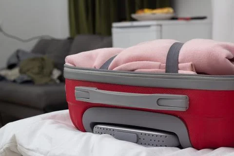 Photo of open red suitcase packed with pink clothes resting on hotel bed Stock Photos