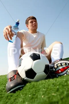 Photo of pensive soccer player seated on green grass-field against blue sky Stock Photos