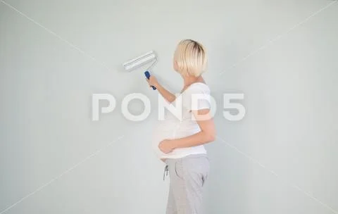 Photo of a pregnant female painting the wall of a bedroom for her future baby. Stock Photos