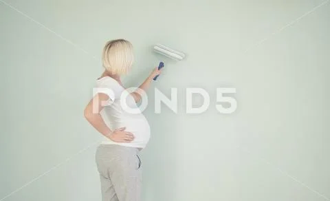 Photo of a pregnant female painting the wall of a bedroom for her future baby. Stock Photos