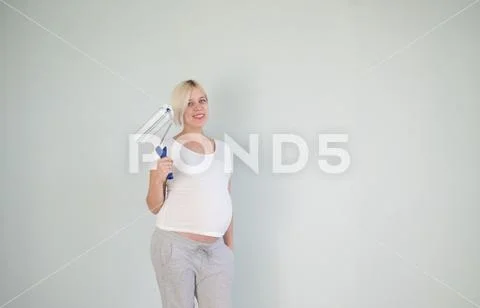 Photo of a pregnant female painting the wall of a bedroom for her future baby. Stock Photos