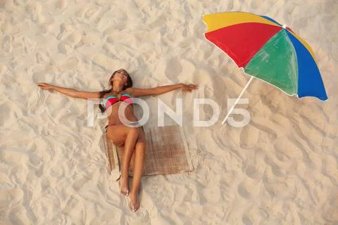 Photo of pretty girl in swimsuit lying on sandy beach with colorful beach umbrel Stock Photos