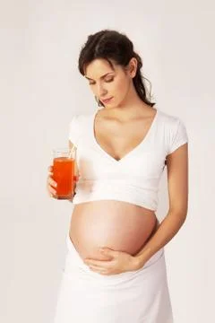 Photo of pretty pregnant woman with glass of juice looking at her belly Stock Photos
