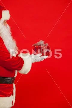 Photo of Santa Claus gloved hand with giftbox, on a red backgrou Stock Photos