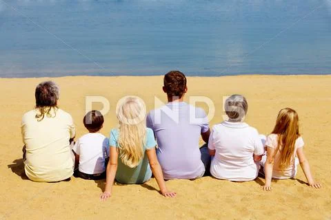 Photo of serene family members sitting on sandy shore and looking at blue water Stock Photos