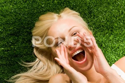 Photo of shouting female lying on green grass and looking at camera Stock Photos