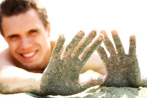 Photo of smiling guy lying on beach and showing his hands covered with sand whil Stock Photos